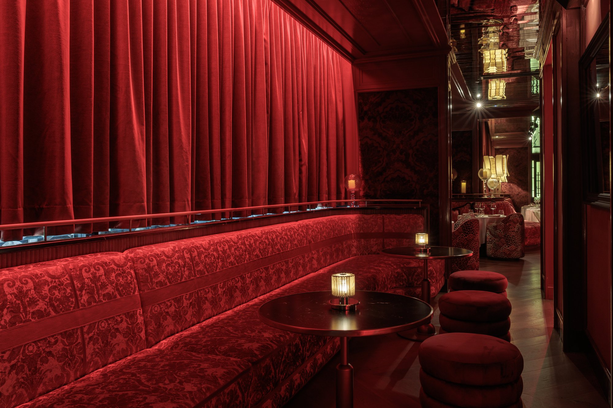 Banqueta de terciopelo rojo y pufs bajo la cortina — Motel · Nuevo, Marbella. Fotografía de Pedro Jaén