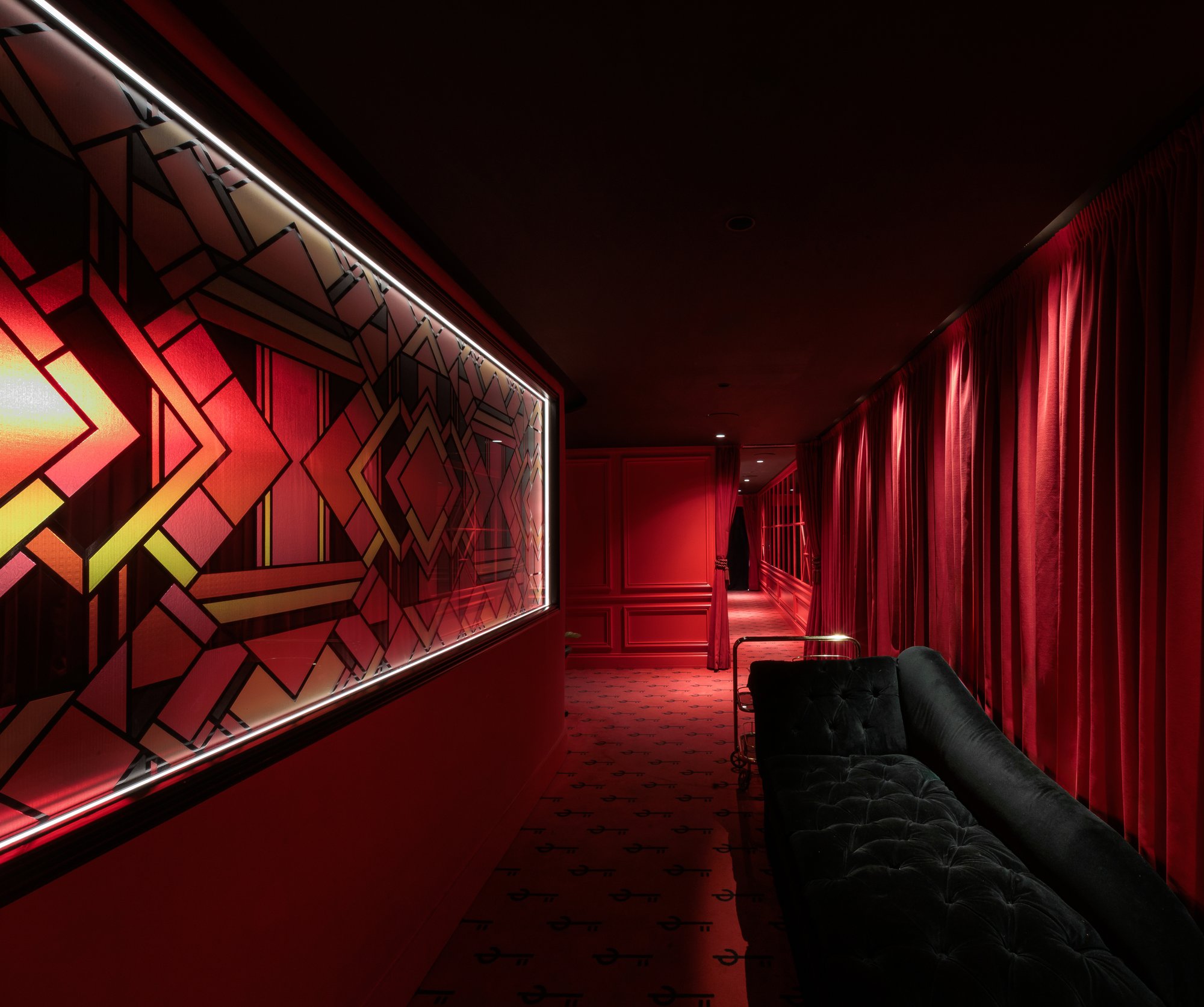 Pasillo con vidriera geométrica iluminada y sofá de terciopelo — Motel, Marbella. Fotografía de Pedro Jaén