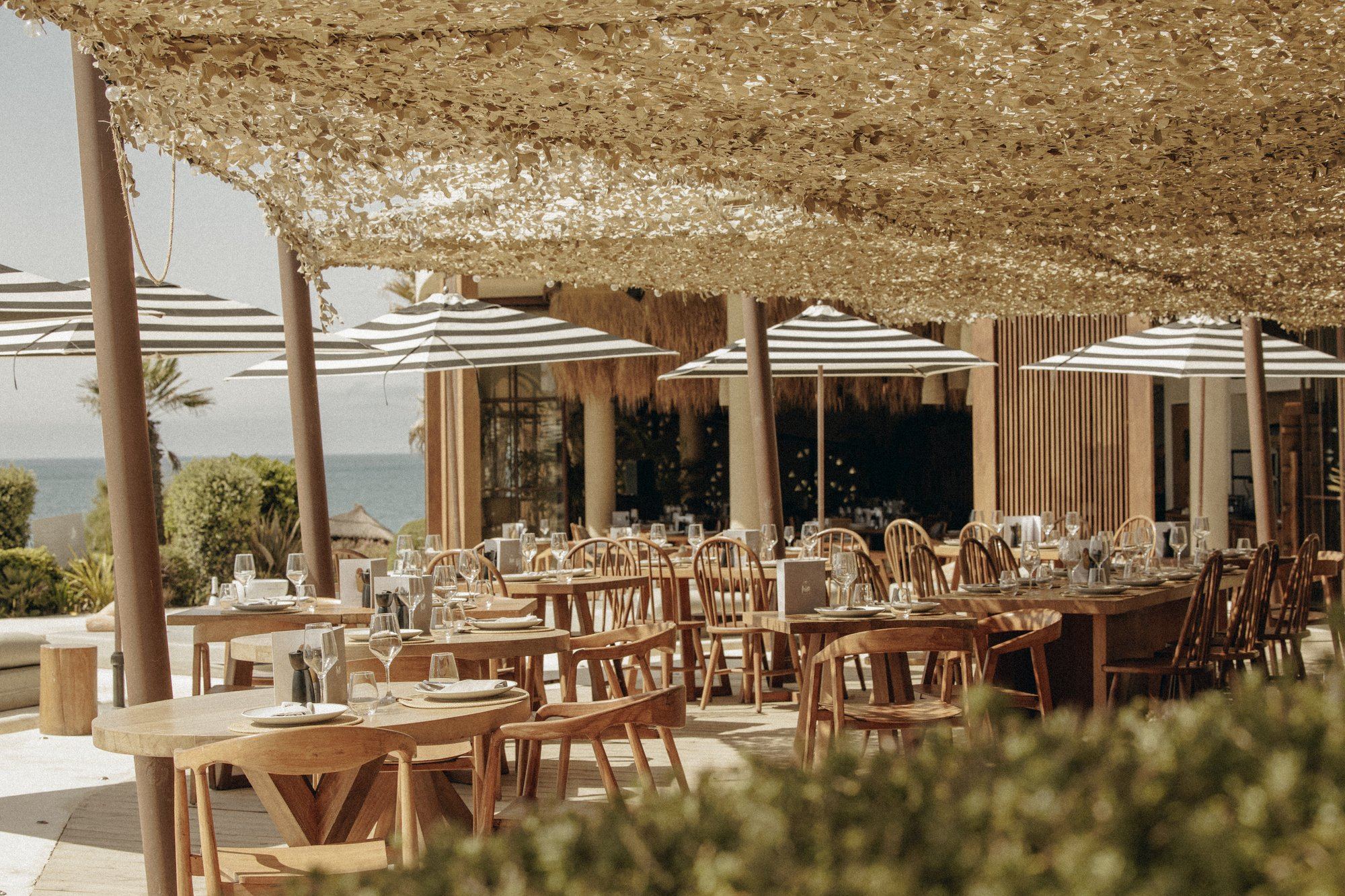Comedor bajo la red de camuflaje y sombrillas de rayas — Nido, Marbella. Fotografía de Pedro Jaén