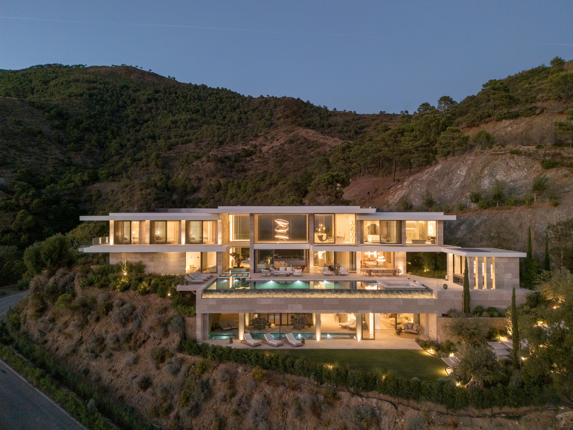Fachada al atardecer con piscina iluminada y vistas a la montaña — Villa Kaizen · La Zagaleta. Fotografía de Pedro Jaén